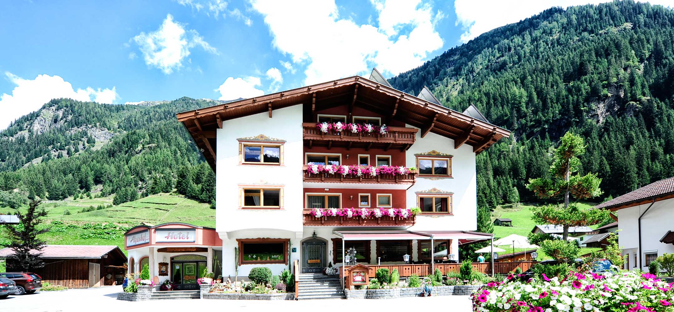 Hausansicht Hotel Alpenhof im Pitztal vor grüner Bergkulisse.